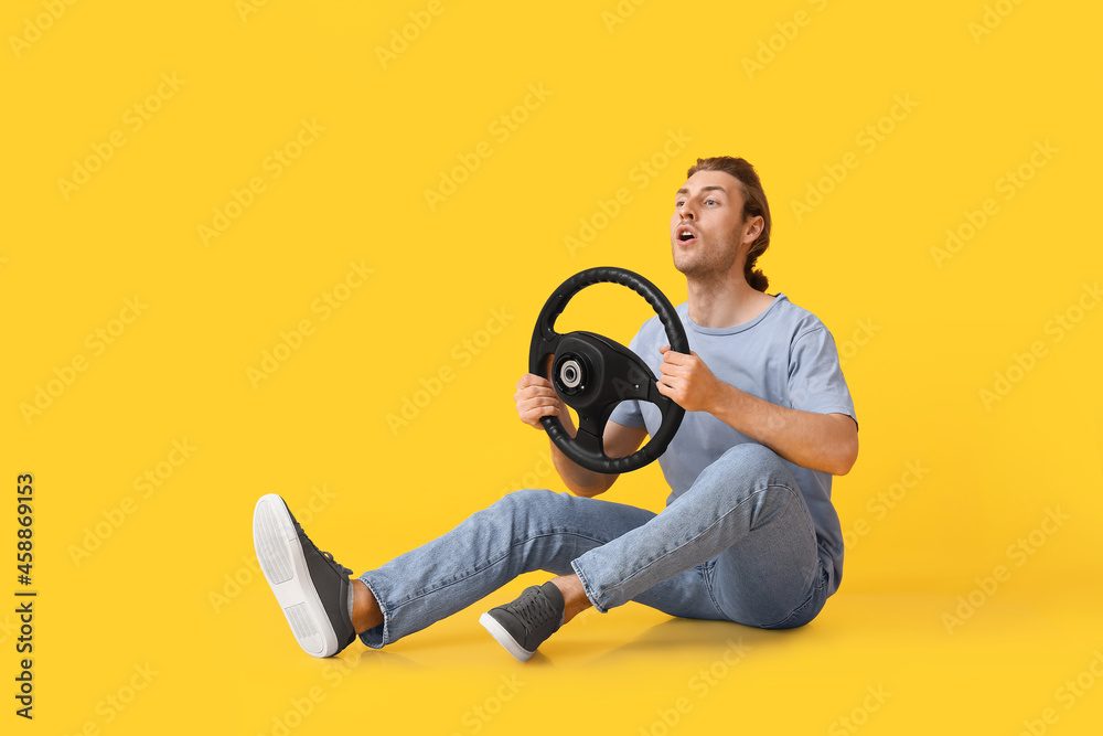 Young man with steering wheel on color background