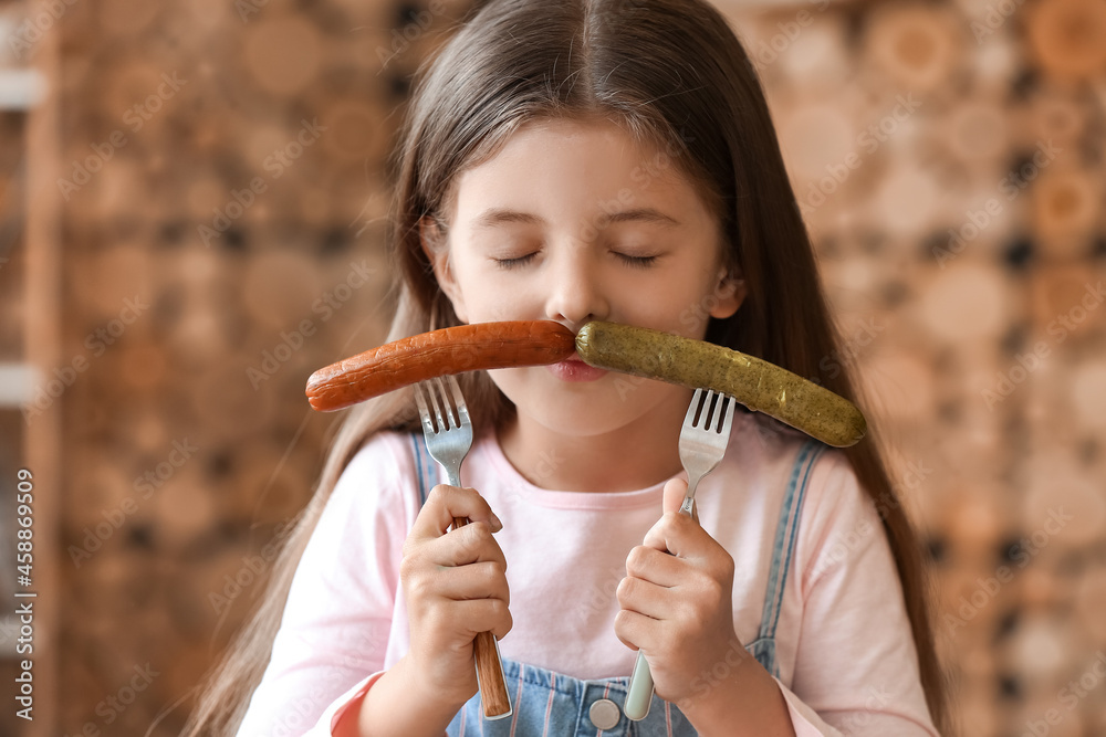 Cute little girl with tasty sausages in kitchen