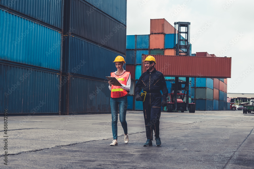 Industrial worker works with co-worker at overseas shipping container yard . Logistics supply chain 