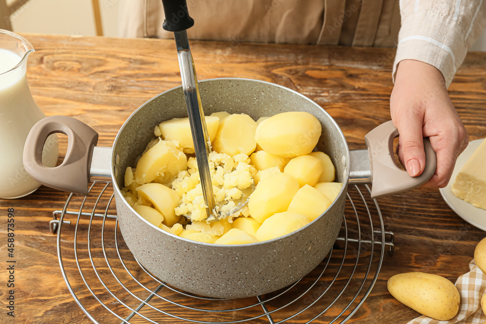 Woman preparing tasty mashed potatoes on table in kitchen, closeup