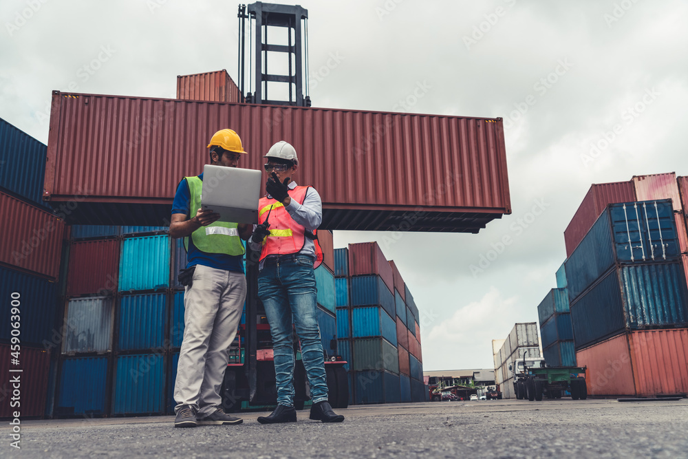 Industrial worker works with co-worker at overseas shipping container yard . Logistics supply chain 