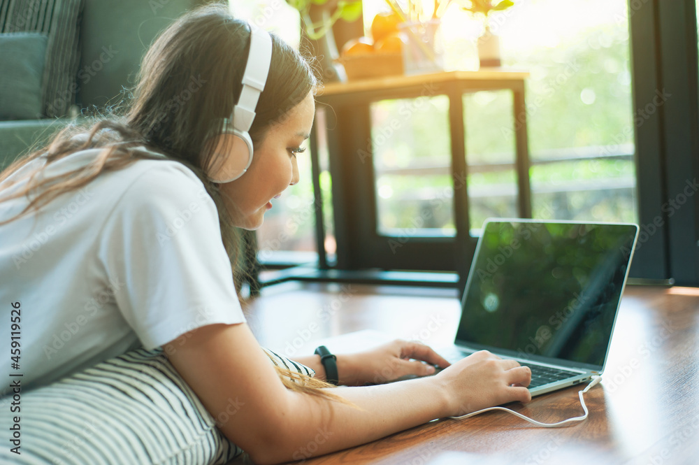 Girl lying on pillow at home watching movies, listening to music from the Internet on laptop.