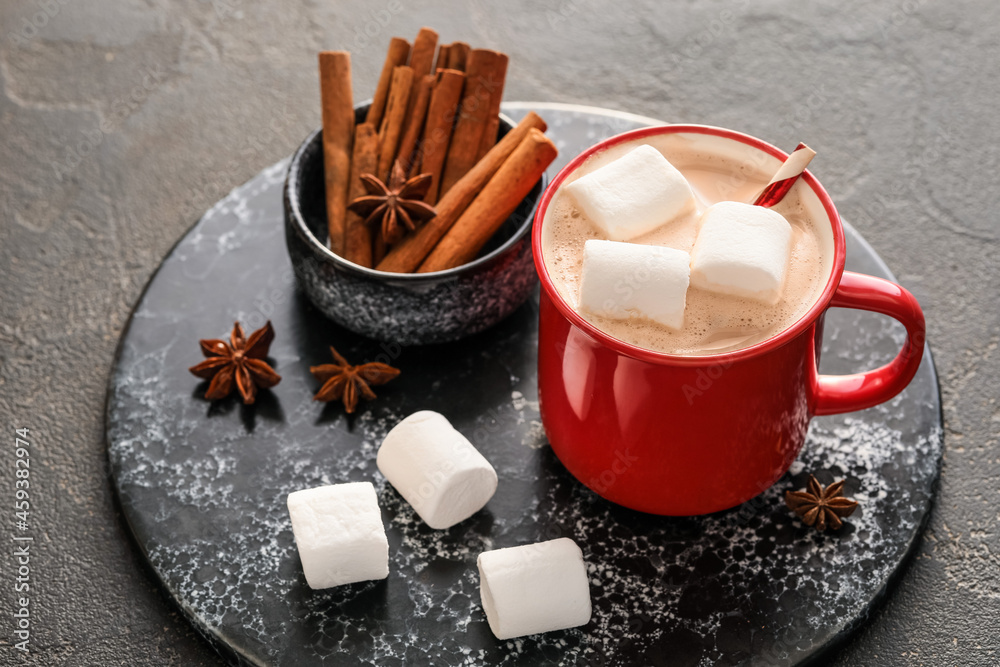 Board with cup of hot cocoa drink and spices on dark background