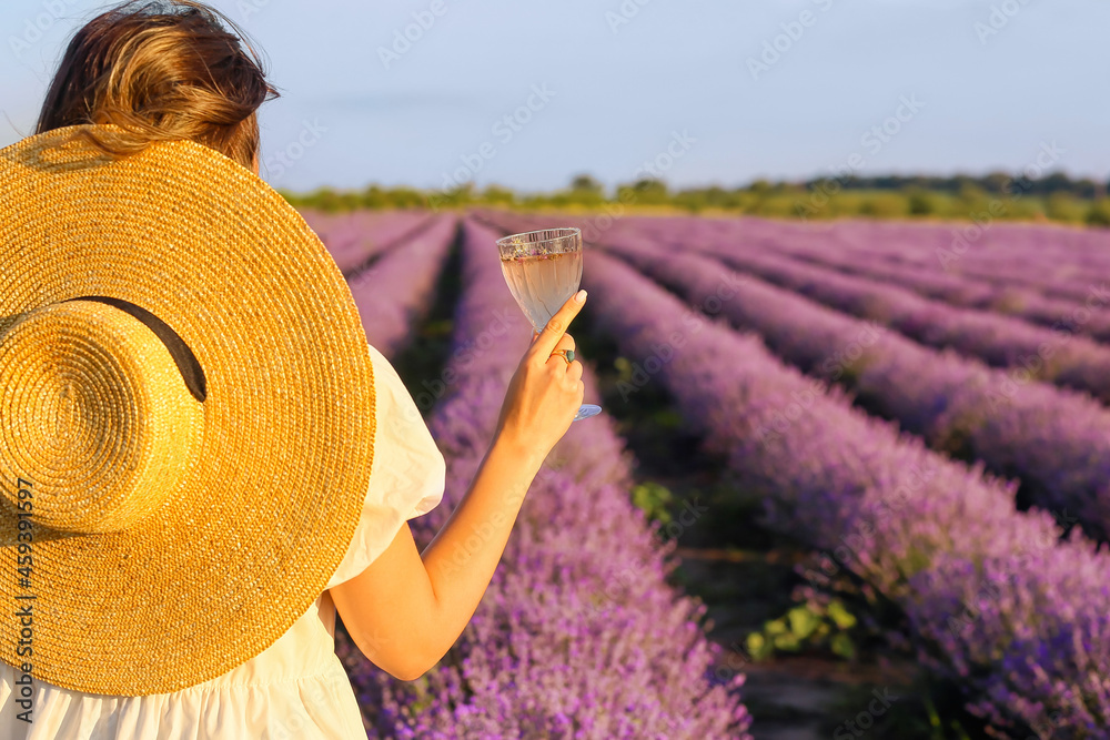 Beautiful young woman drinking wine in lavender field