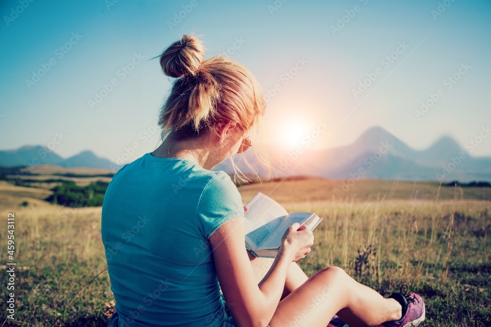 Woman holds book in her hands. Reading the book in a nature during beautiful sunset.