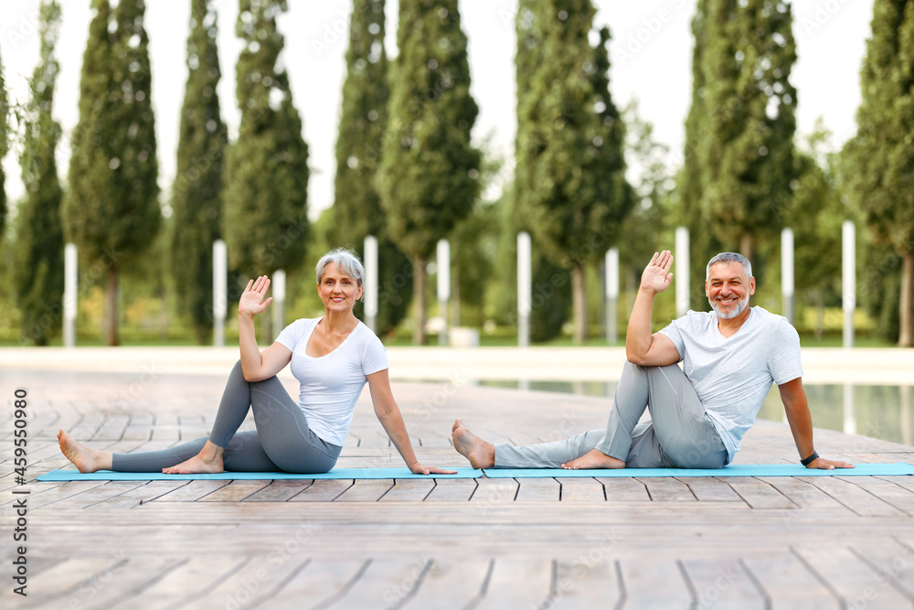 Happy senior retired couple doing partner yoga outside in city park