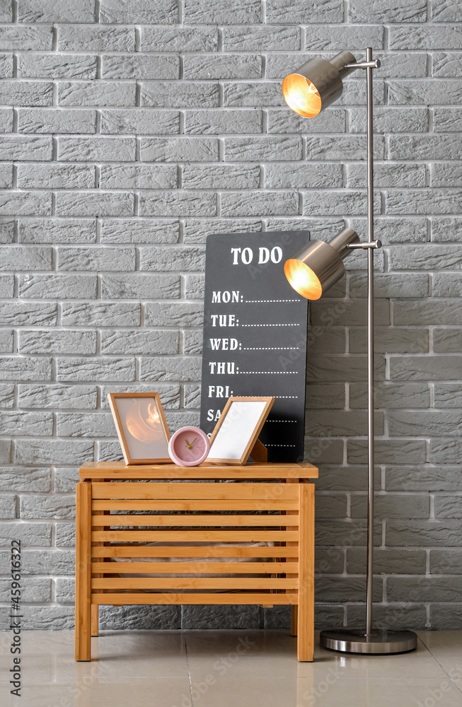 Table with photo frames, alarm clock and lamp near brick wall