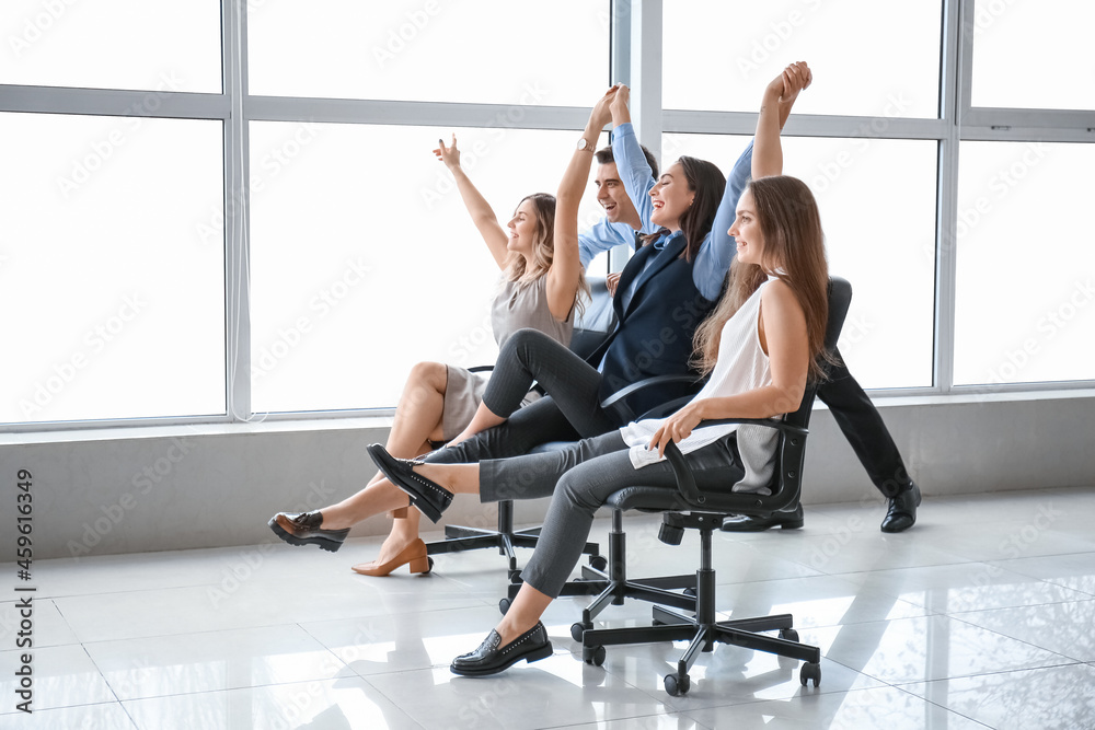 Happy colleagues riding chairs in office