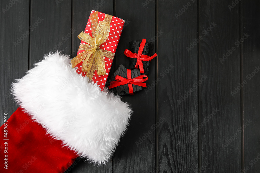 Christmas sock with coal and gift on dark wooden background