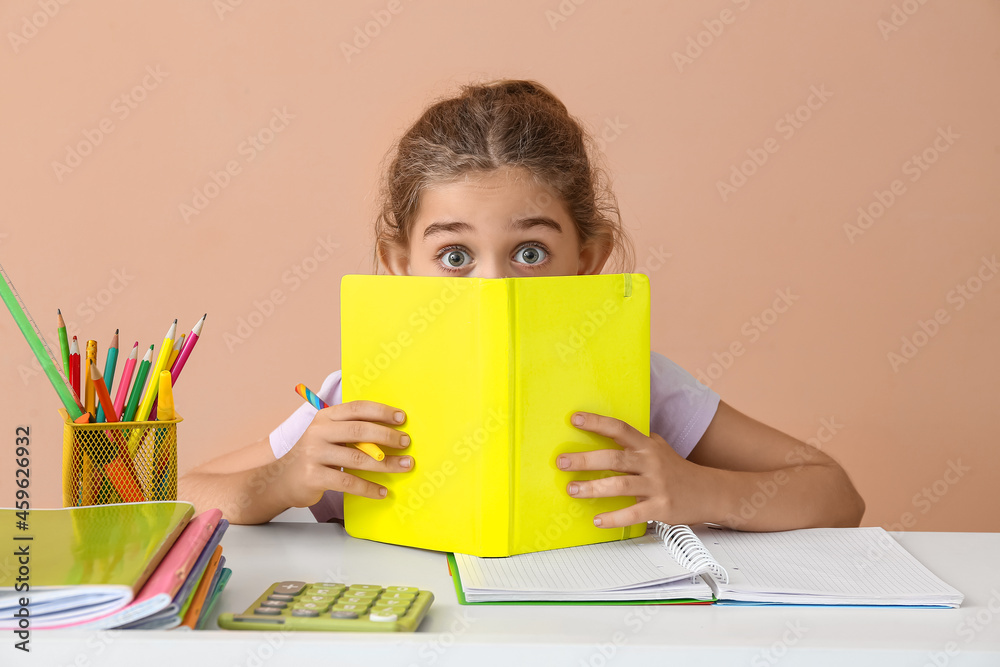 Little girl doing homework at table on color background