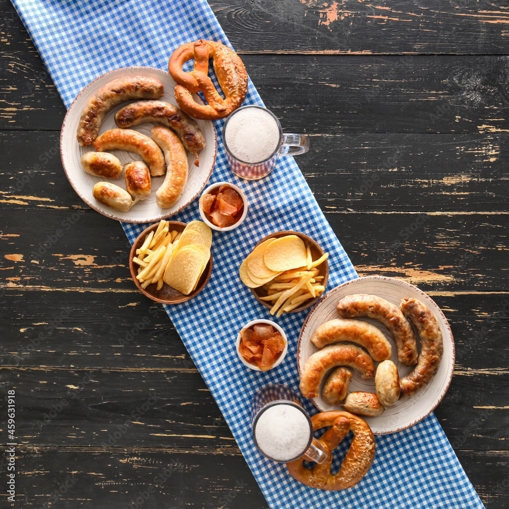 Mugs of cold beer, plates with Bavarian sausages and snacks on black wooden background. Oktoberfest 