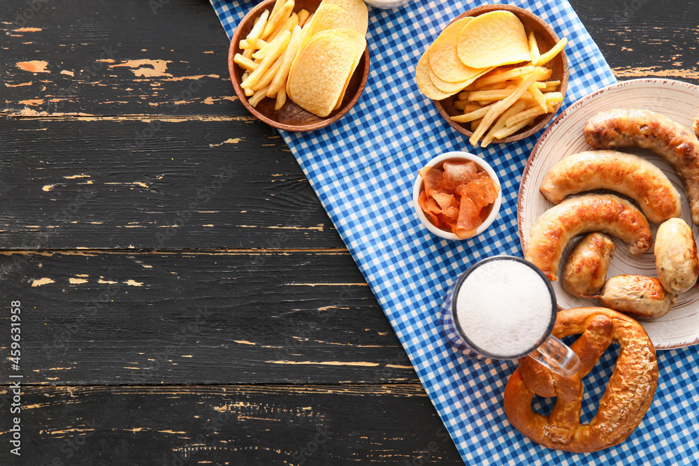 Mug of cold beer, plate with Bavarian sausages and snacks on black wooden background. Oktoberfest ce