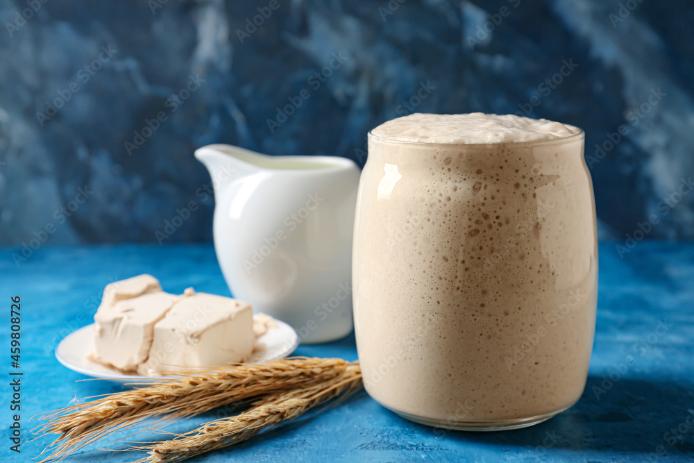 Glass jar with fresh sourdough on blue background