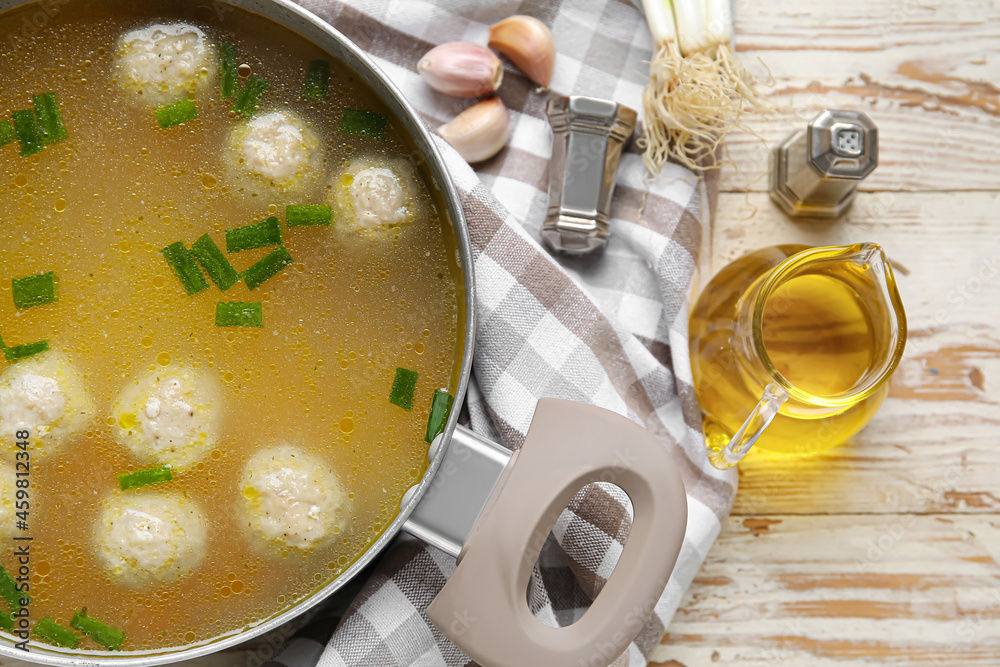 Pot with tasty meatball soup and spices on light wooden background, closeup