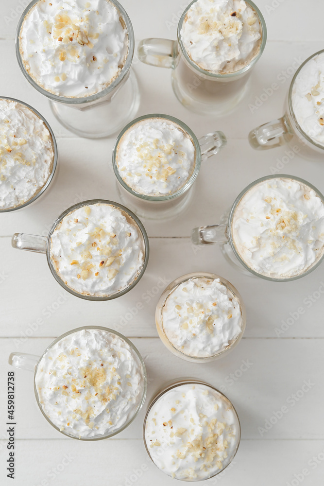 Glasses and cups of tasty latte with nuts on white wooden background