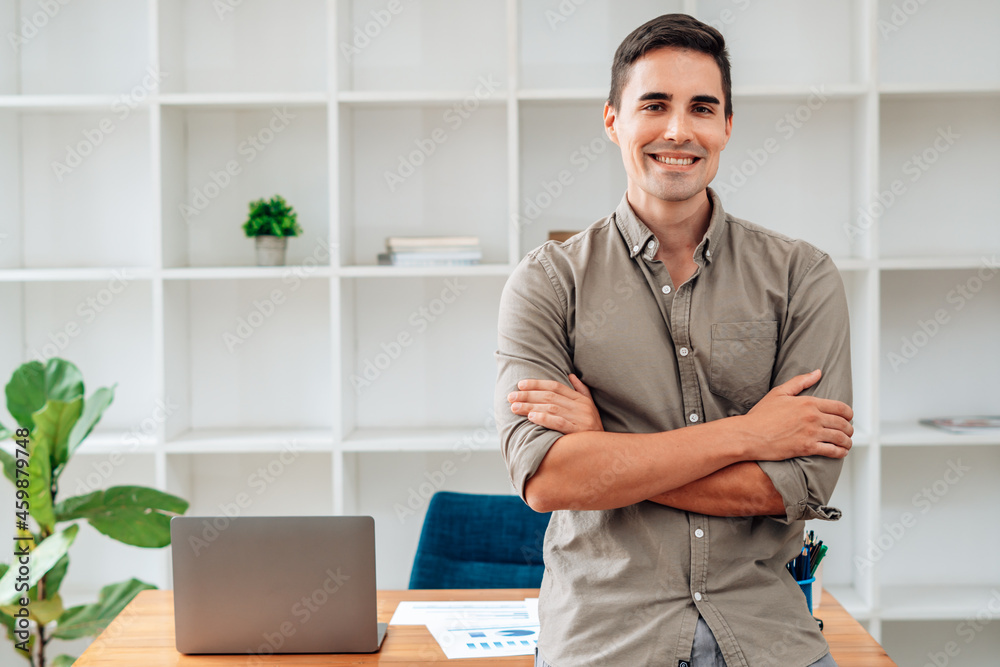 Portrait of happy man stand at office desk, looking at camera, smiling.