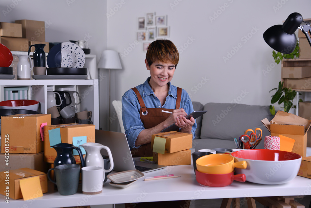 Mature Asian woman entrepreneur, Business owner working on digital tablet checking address and deliv