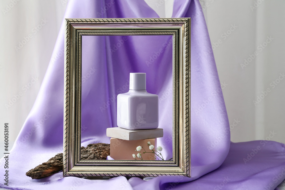 Composition with stylish bottle of perfume and frame on color cloth background