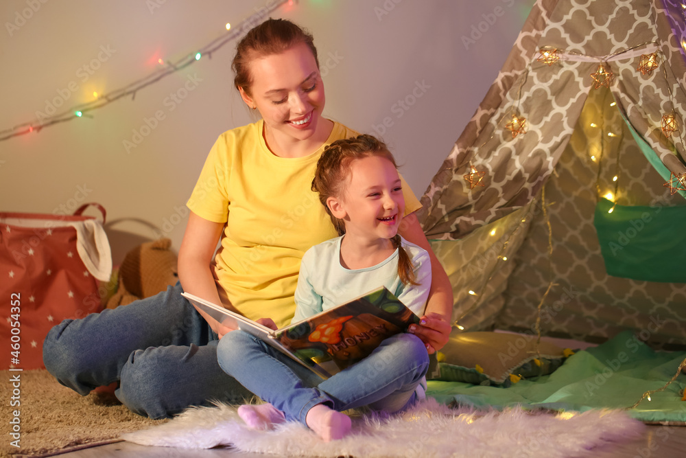 Young woman reading fairy-tale to her little daughter late in evening at home