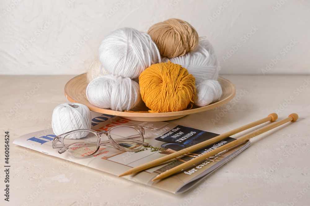 Wooden plate with knitting yarn, needles, eyeglasses and magazine on light table