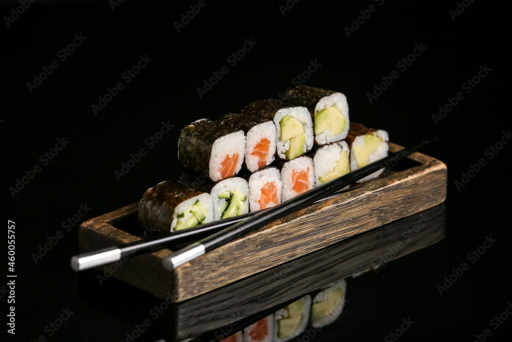 Wooden tray with delicious maki rolls and chopsticks on dark background