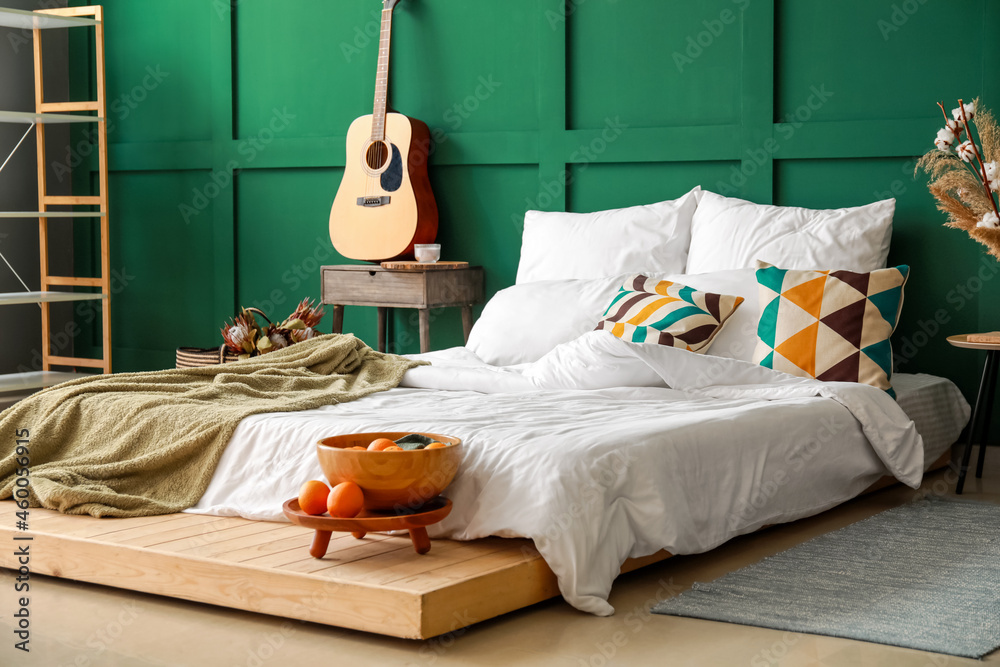 Comfortable bed with soft linens and wooden bowl with fruits near color wall