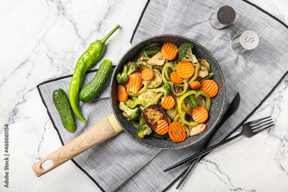 Frying pan with different vegetables and spices on light background