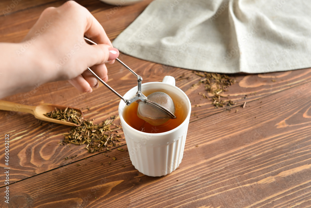 Woman preparing tasty hojicha green tea on wooden background, closeup