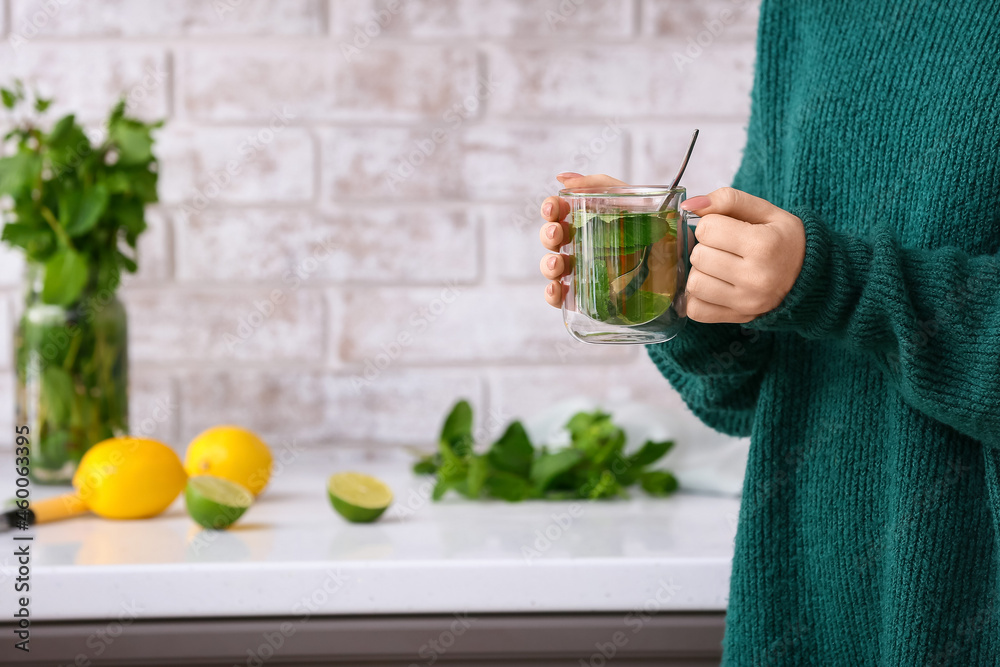 Woman with glass cup of tasty mint tea in kitchen