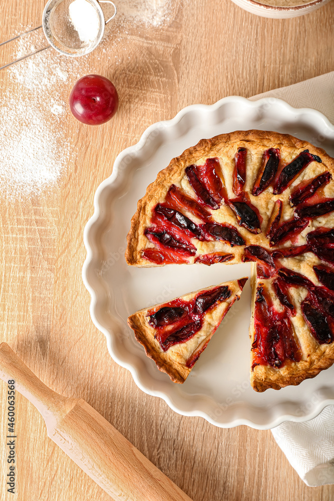 Baking dish with tasty plum pie on wooden background