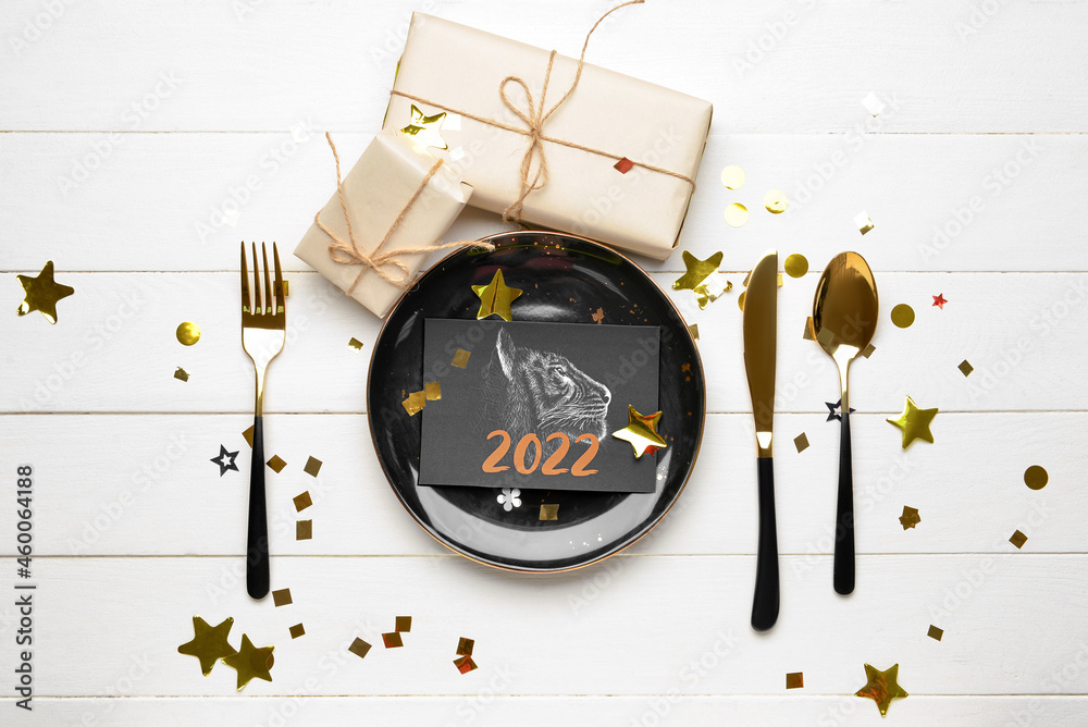 Table setting with greeting card for New Year 2022 celebration on white wooden background