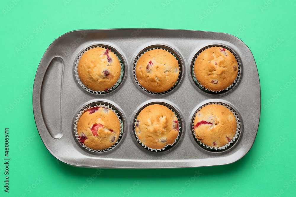 Baking tin with tasty cranberry muffins on color background