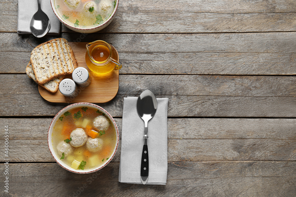 Bowls with tasty meatball soup, bread and spices on wooden background