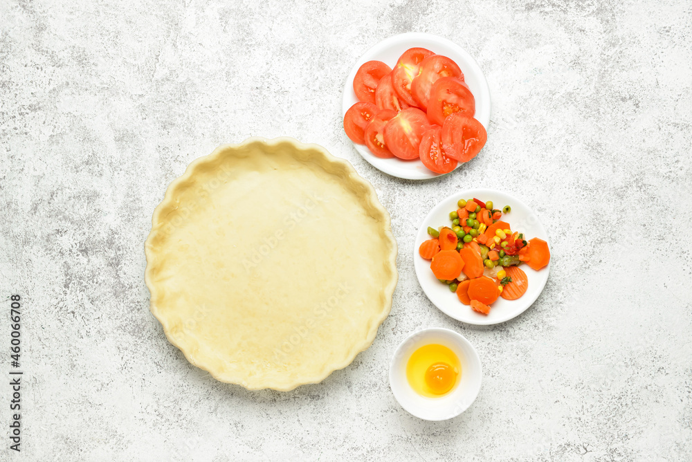 Raw dough and fresh vegetables for preparing pot pie on light background