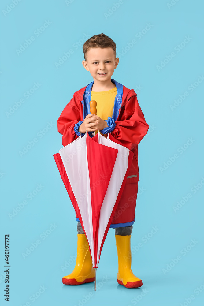 Cute little boy in raincoat and with umbrella on color background