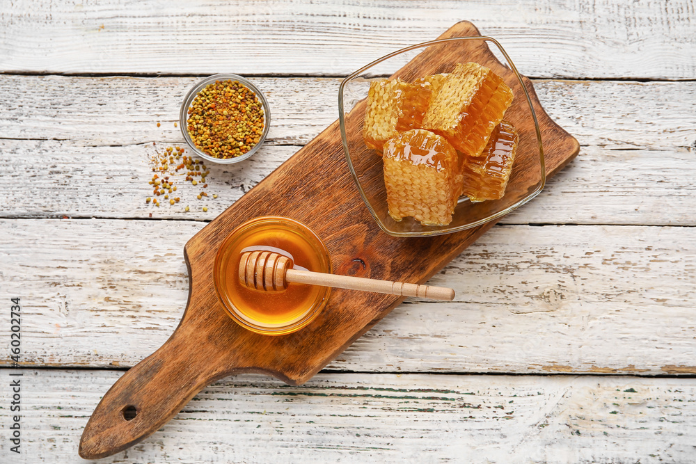 Bowls of honey, combs and bee pollen on white wooden background