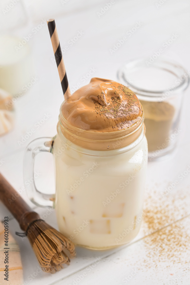 Mason jar of tasty dalgona hojicha latte and chasen on light wooden background