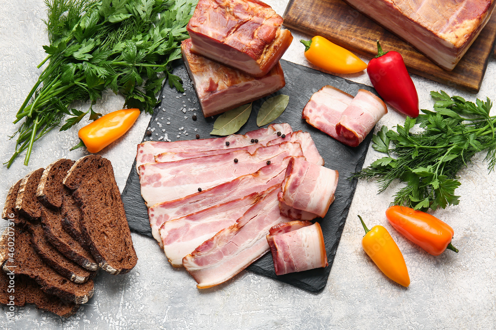 Board with slices of tasty smoked bacon, bread and fresh vegetables on light background