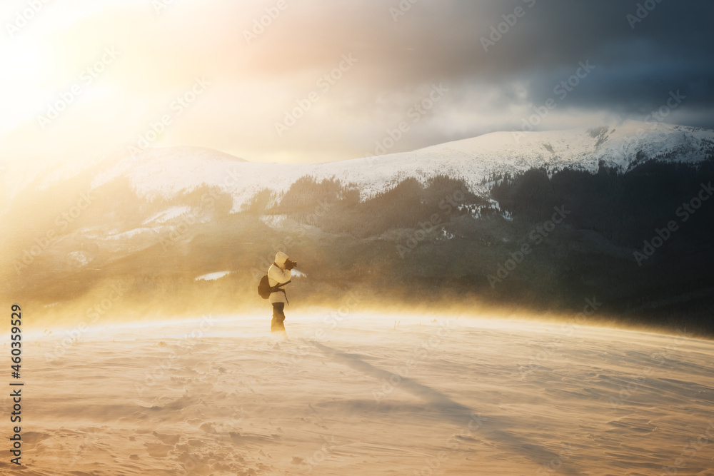 Alone photographer on mountain top in snowstorm with a backpack in winter time. Travel concept. Carp