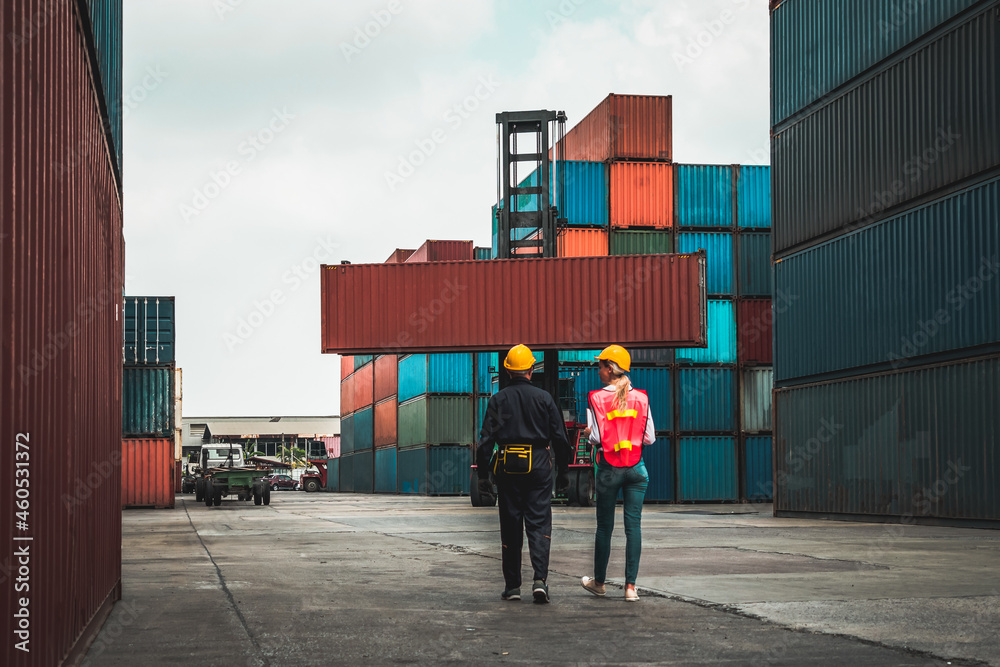 Industrial worker works with co-worker at overseas shipping container yard . Logistics supply chain 