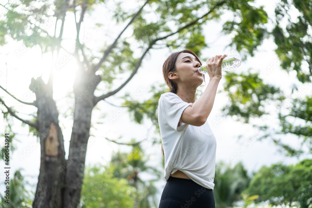 亚洲年轻女运动员在公园锻炼后喝了一瓶水。