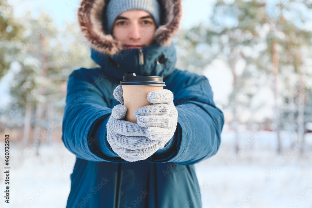 Young man with cup of hot tea on snowy day, closeup