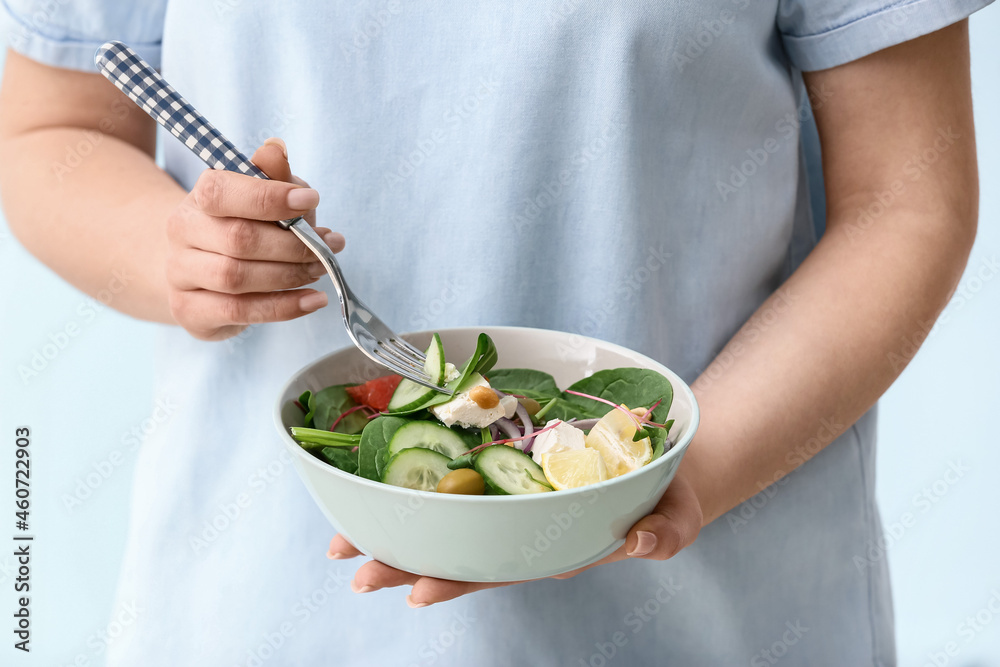 Woman eating healthy salad on light background, closeup