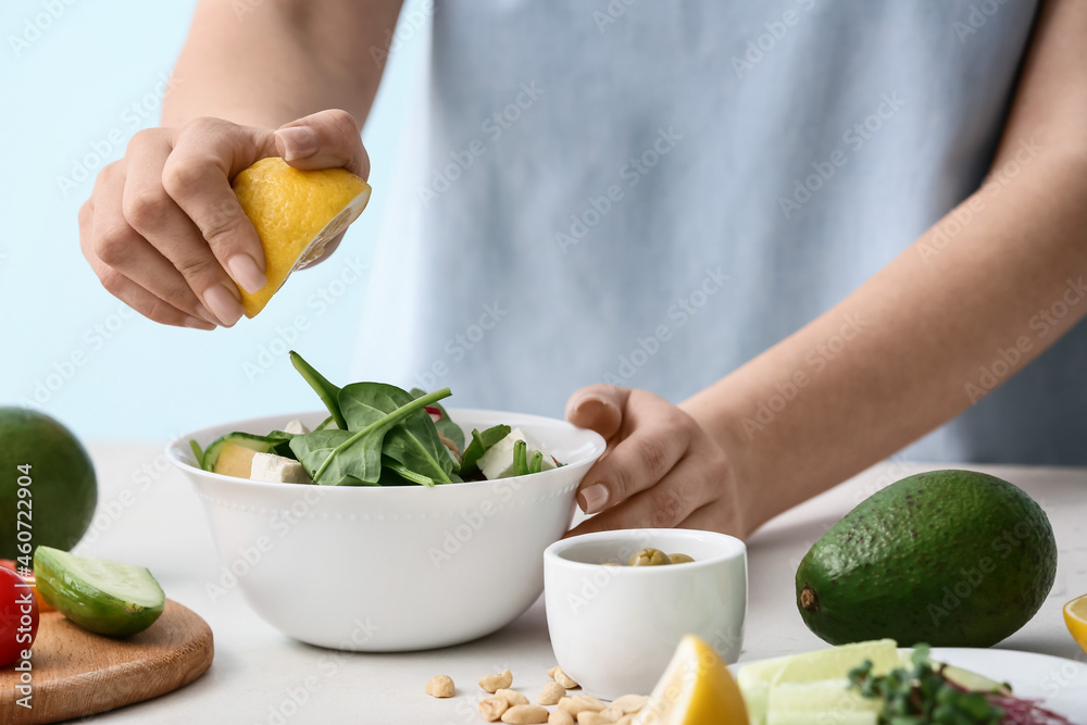 Woman squeezing lemon in healthy salad on table in kitchen