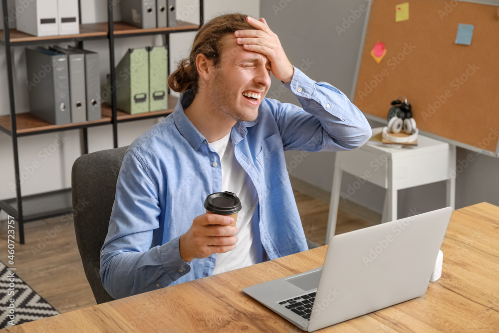 Handsome young man with cup of coffee video chatting in office