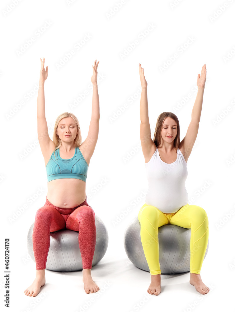 Young pregnant women with fitball practicing yoga on white background