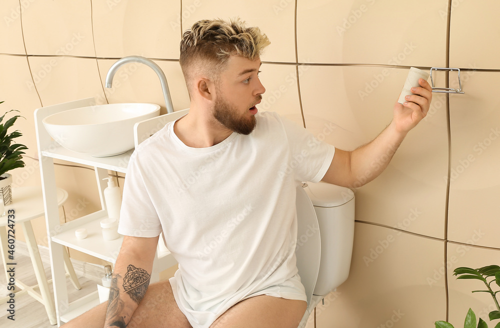 Shocked young man out of toilet paper in bathroom