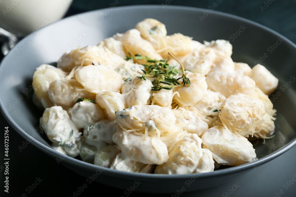 Bowl of tasty gnocchi with creamy sauce on black background, closeup