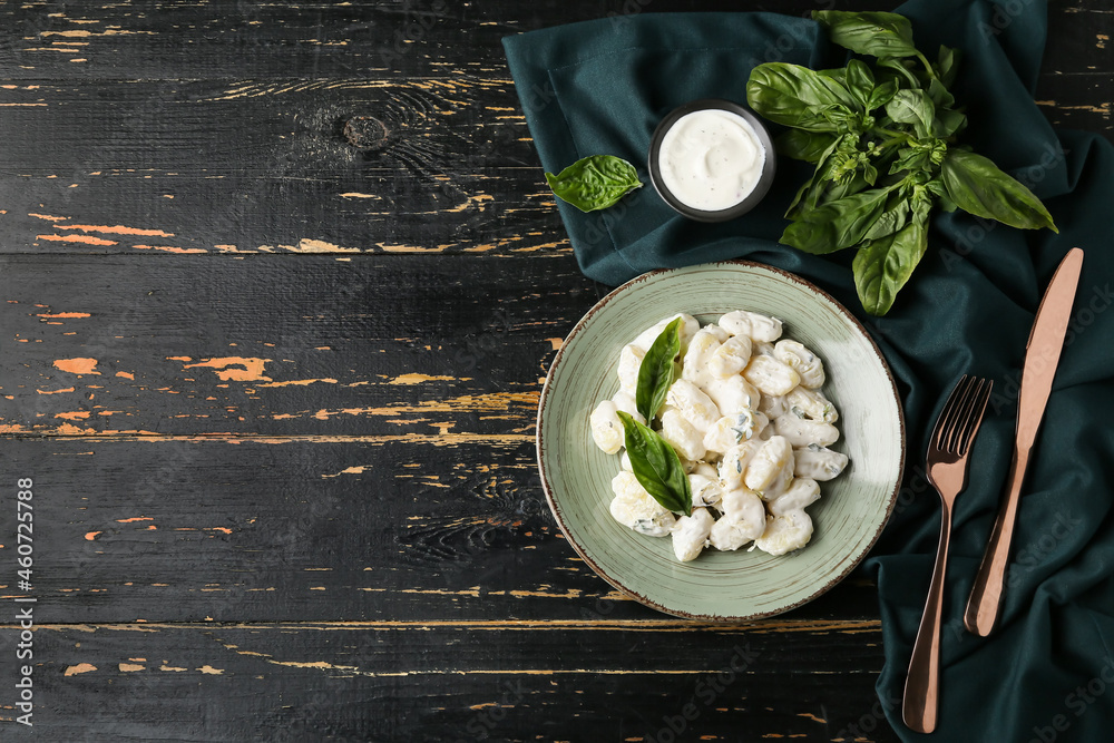 Plate of tasty gnocchi with creamy sauce on black wooden background