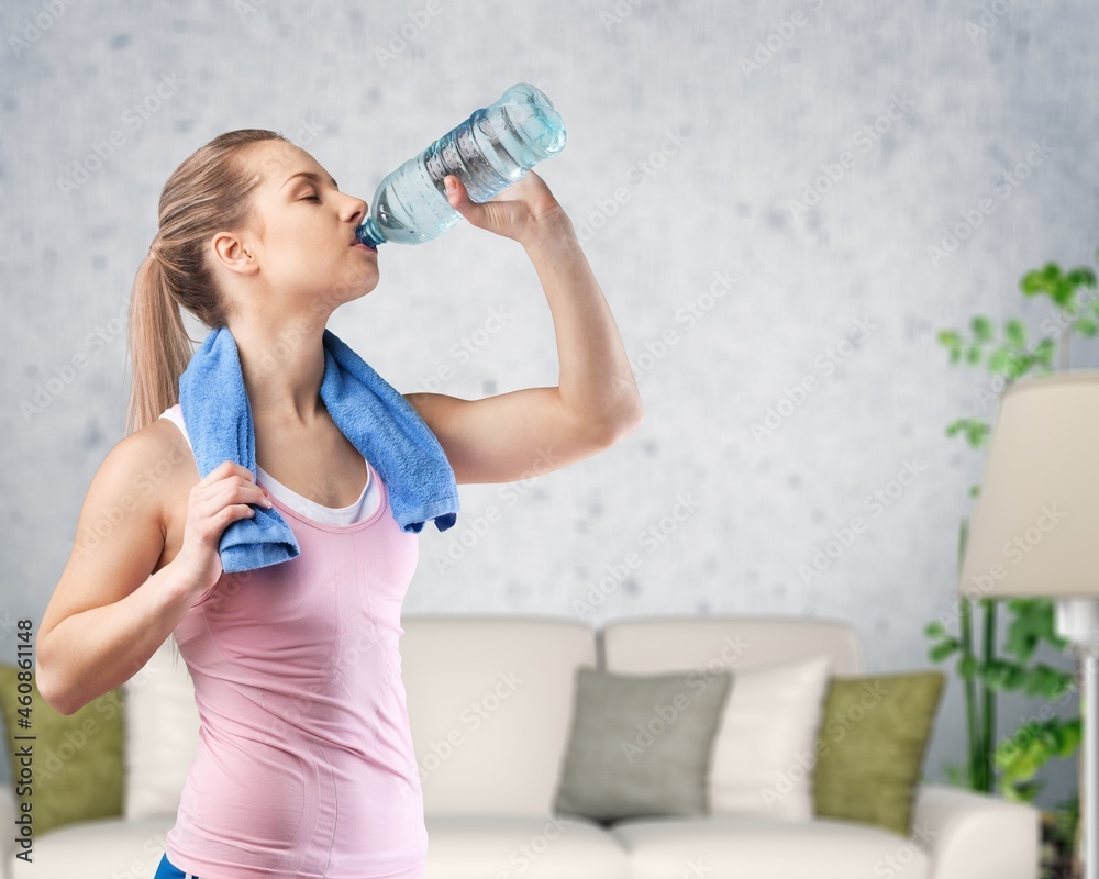 Pretty woman in sports clothes drinking water or protein shake from the bottle at home.